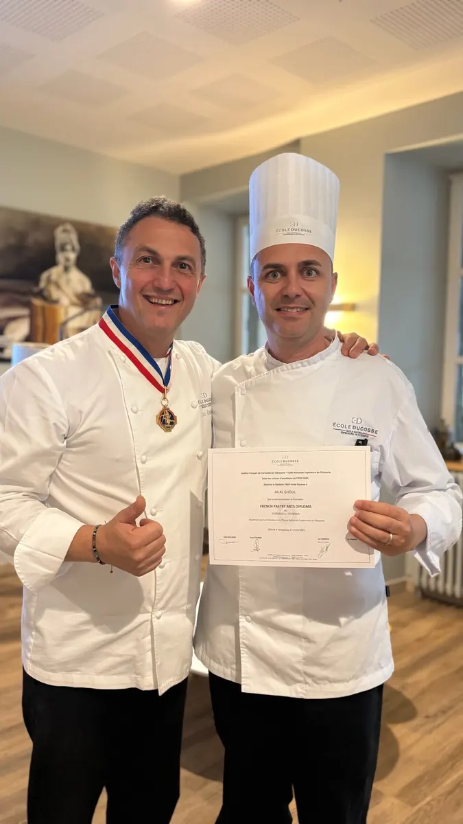 Ali Al Ghoul receiving his French Pastry Arts Diploma at École Ducasse, Paris, alongside a Meilleur Ouvrier de France instructor in tricolor MOF collar.