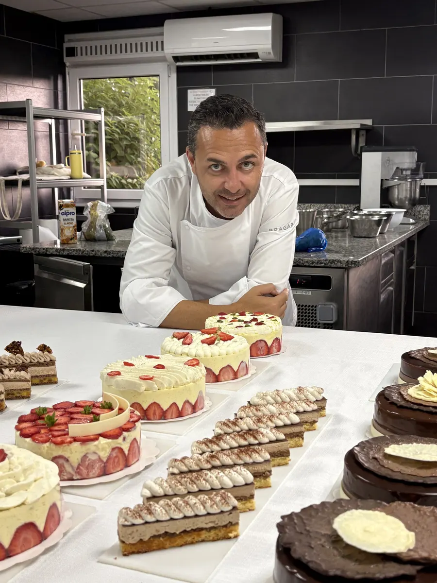 Ali Al Ghoul standing behind a long table of patisserie — fraisiers, opera cake, individual entremets — at École Ducasse.