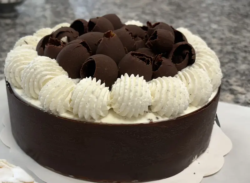 Ali's Forêt-Noire — chocolate cake banded in dark ganache, crowned with hand-piped vanilla cream rosettes and a mound of curled chocolate shells.