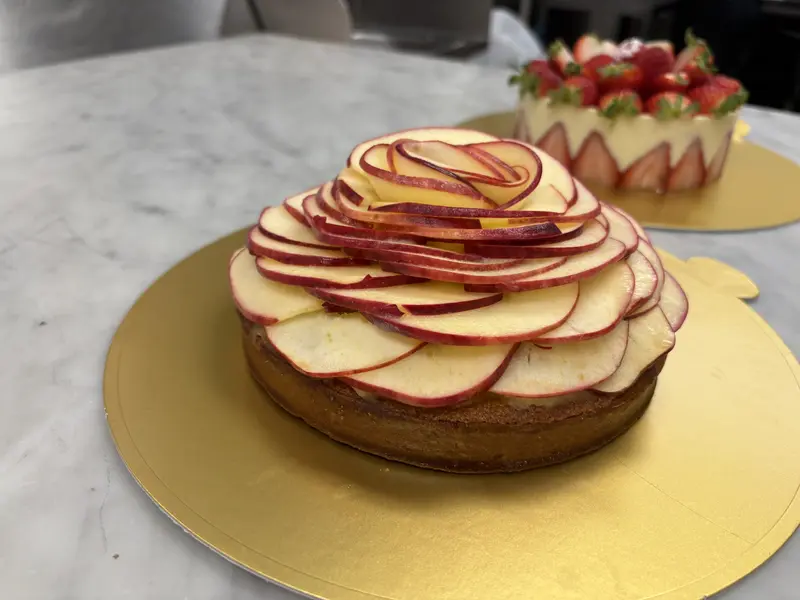 Ali's tall apple rose tart — thin red-skinned apple slices stacked into a domed flower bloom on a sablé base, on a gold board.