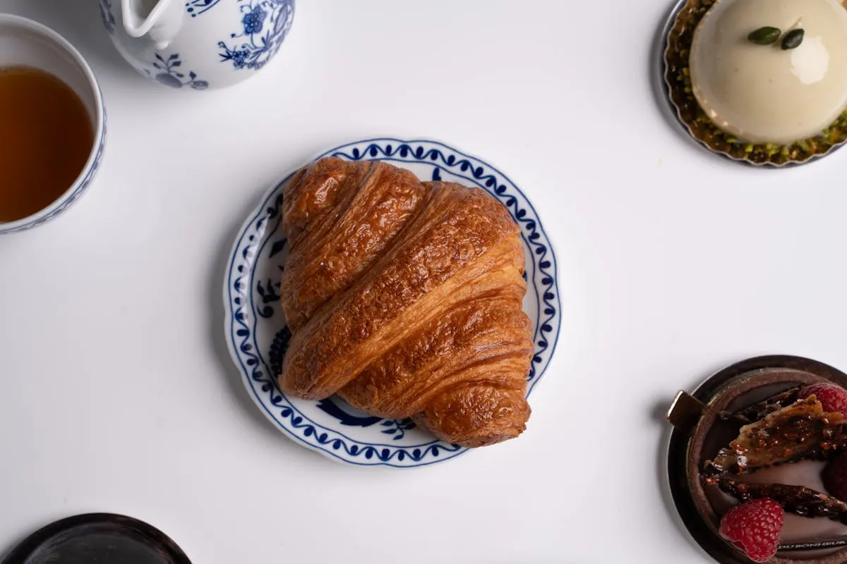 A perfect golden croissant on a blue-and-white printed plate beside a cup of tea.