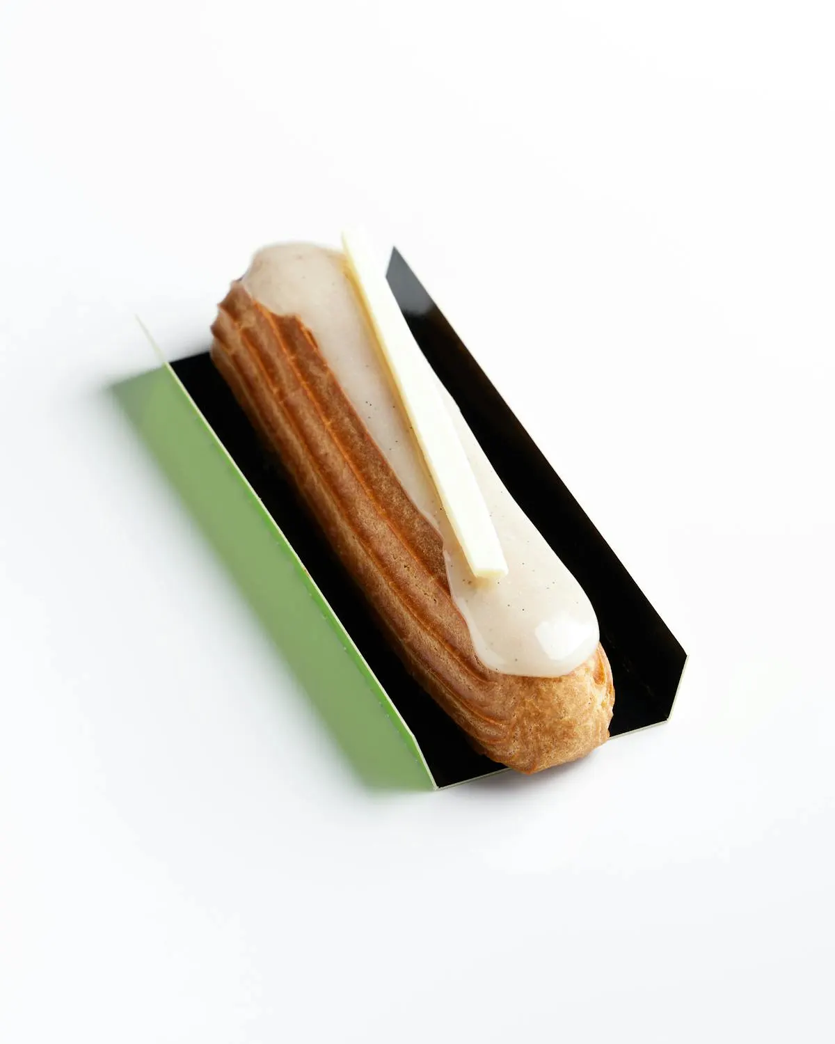 A single vanilla éclair with a glossy cream glaze on a green-and-black presentation board.