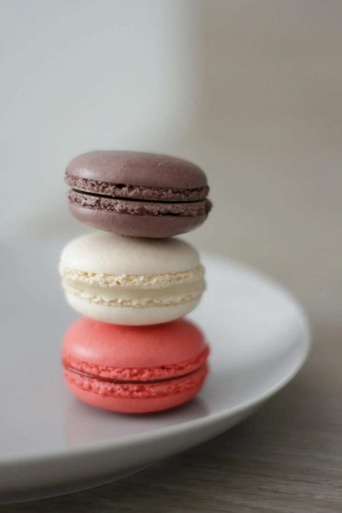 A stack of three macarons — chocolate, vanilla, and pink — on a white plate.