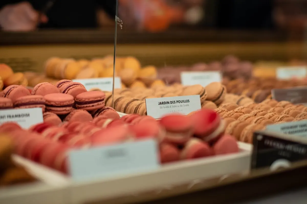 Pink and beige French macarons displayed in a Paris bakery case behind glass.