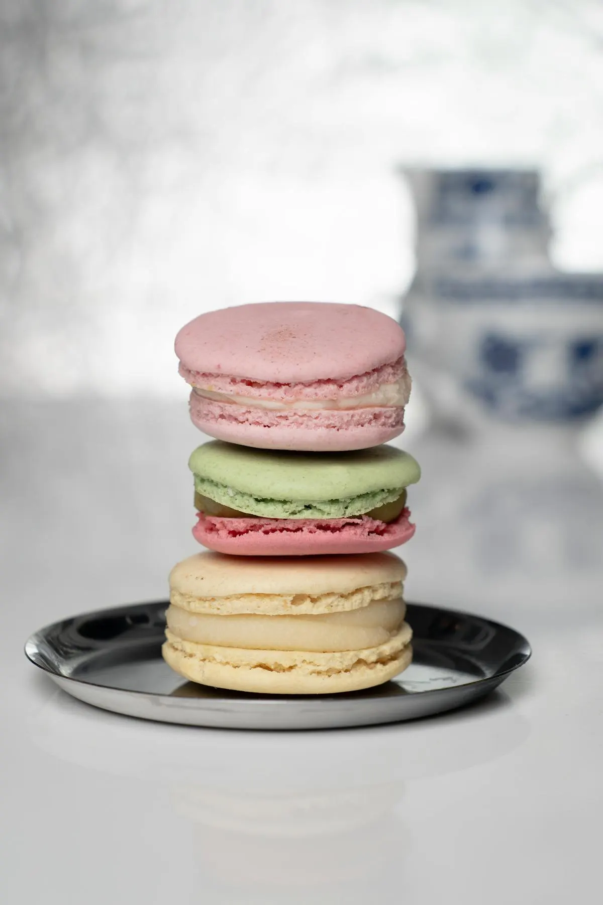 A stack of three pastel macarons — pink, light green, and vanilla — on a dark plate.