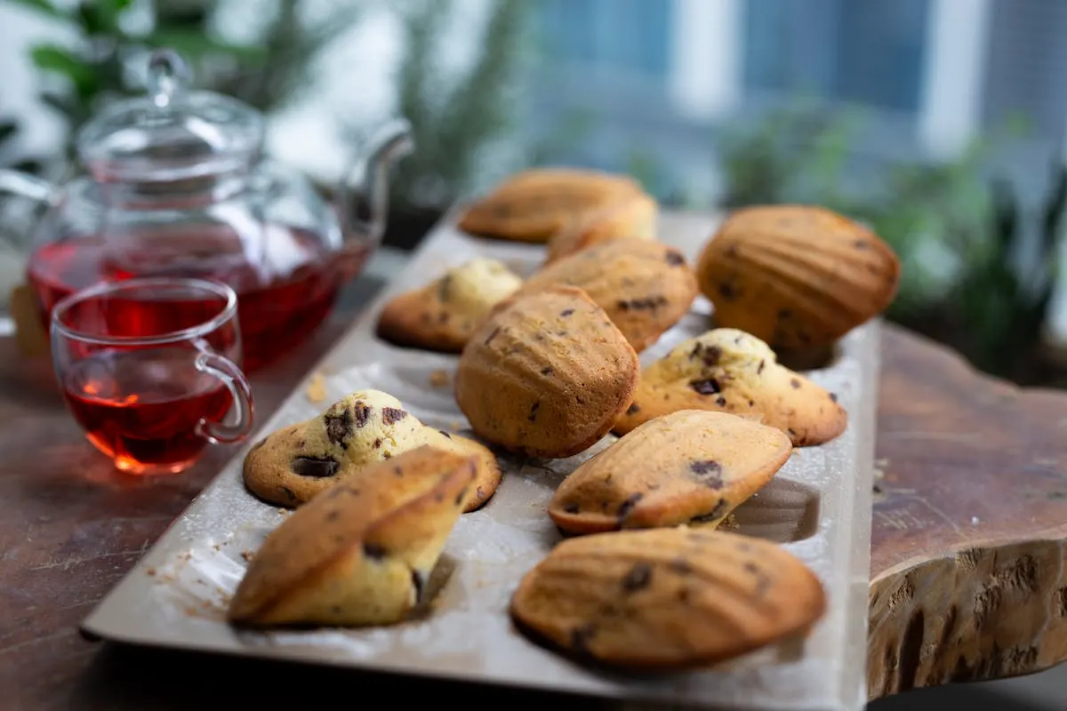 Chocolate-chip madeleines on a wooden tray with a glass teapot of red tea.