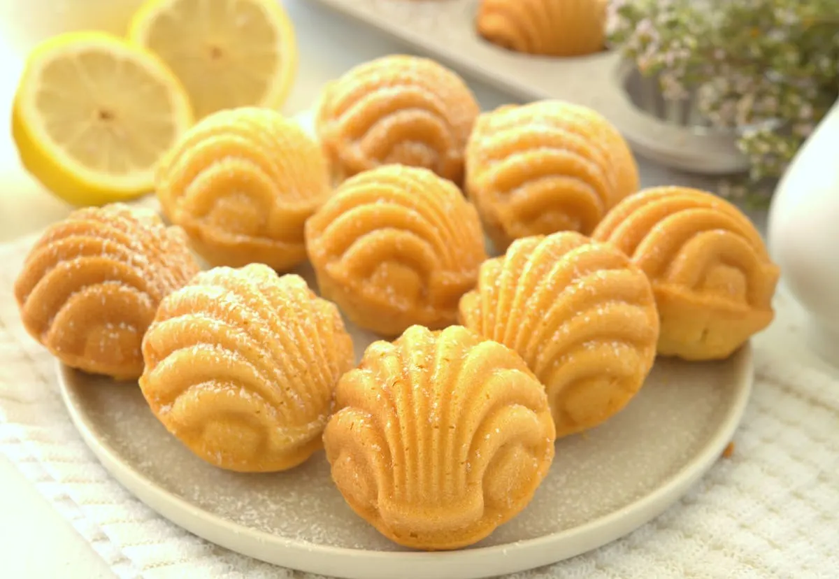 Madeleines dusted with powdered sugar, beside fresh lemon halves.