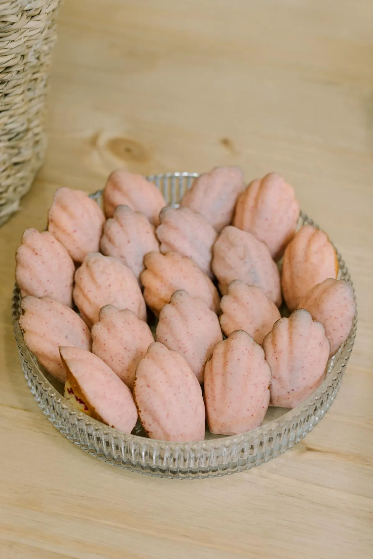 Madeleines coated in a rose-pink raspberry glaze, displayed in a glass dish.