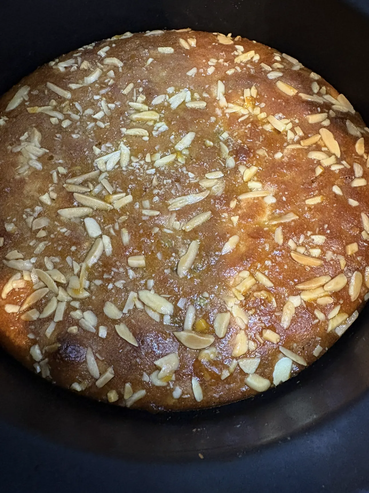 Ali's gluten-free orange and pistachio cake — a deep golden round, glazed and covered edge to edge with slivered nuts, photographed from above.