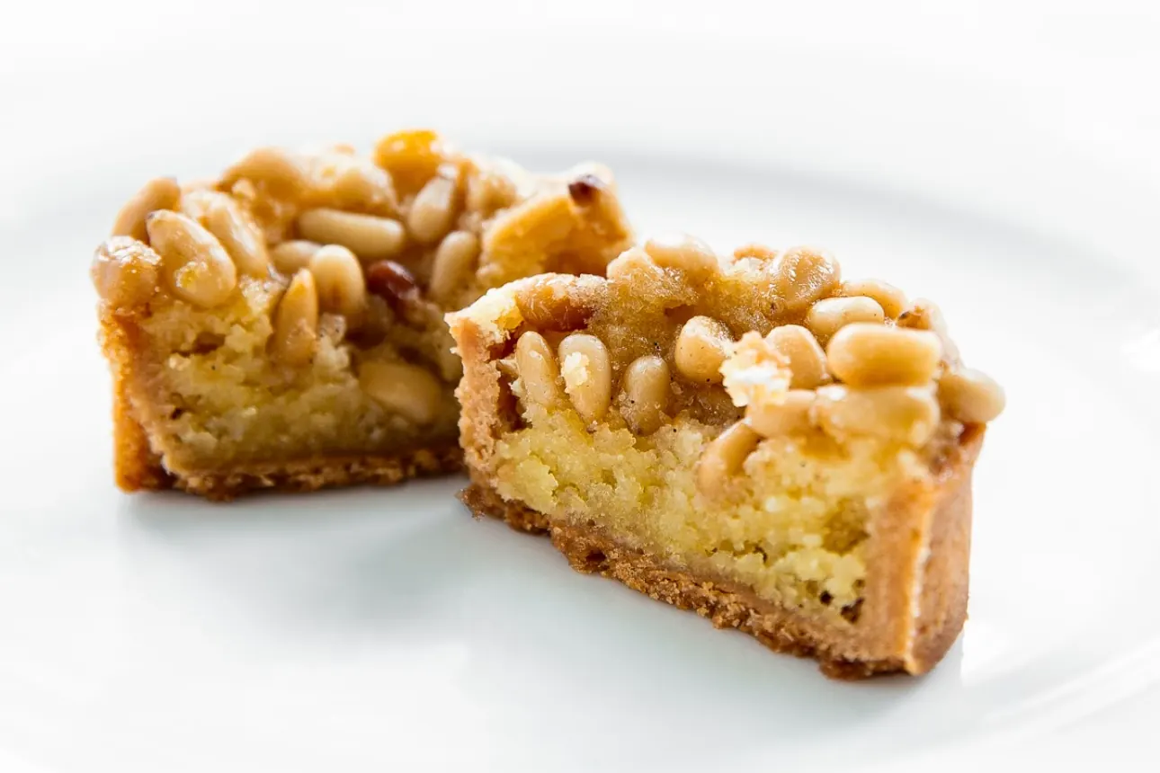 The same pine-nut tart cut in half, showing the almond cream filling under the layer of pine nuts and the thin crisp base.