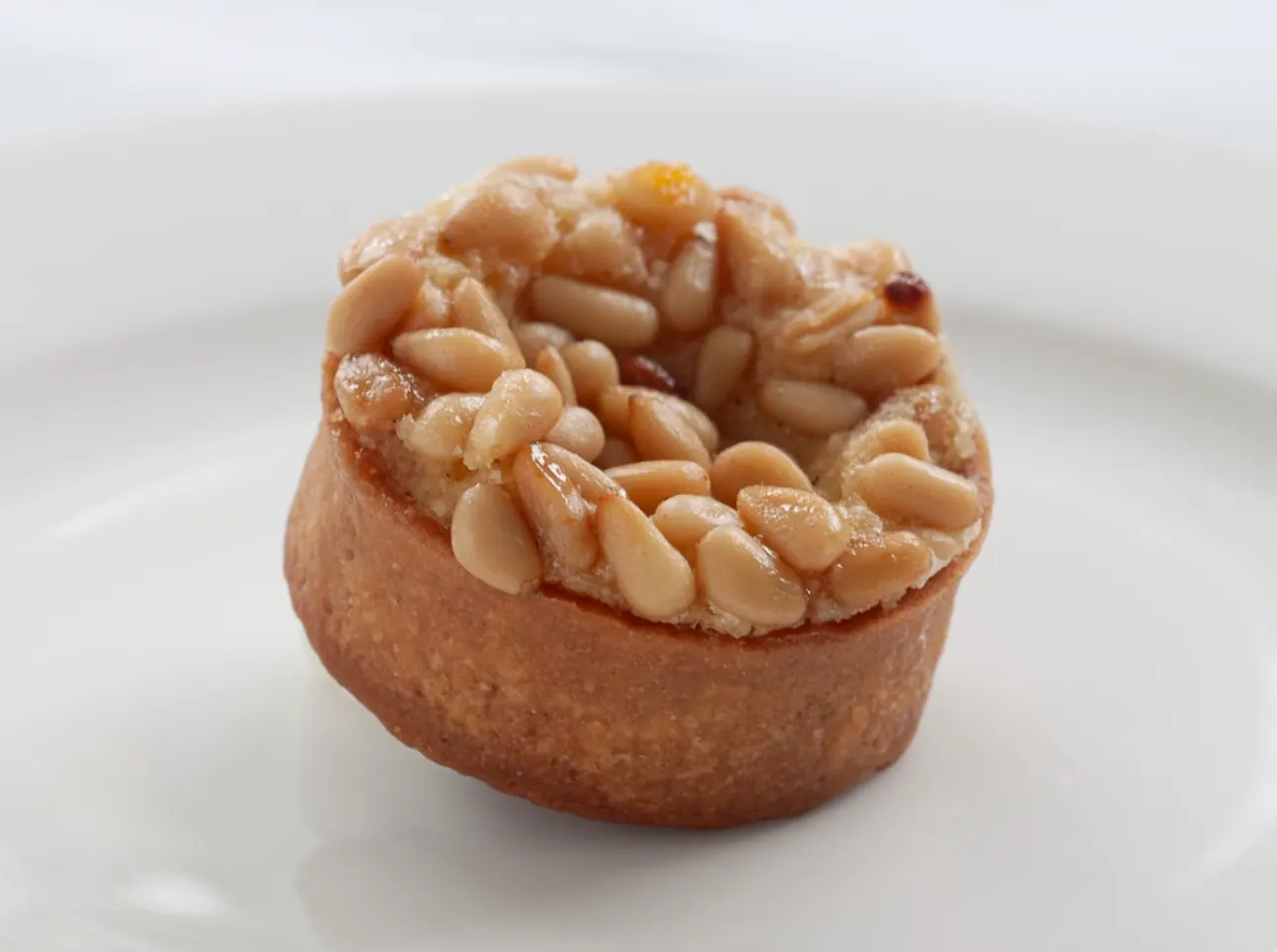 Ali's pine-nut tart — whole toasted pine nuts glazed and crowded across the top of a deep golden sablé shell, on a white plate.
