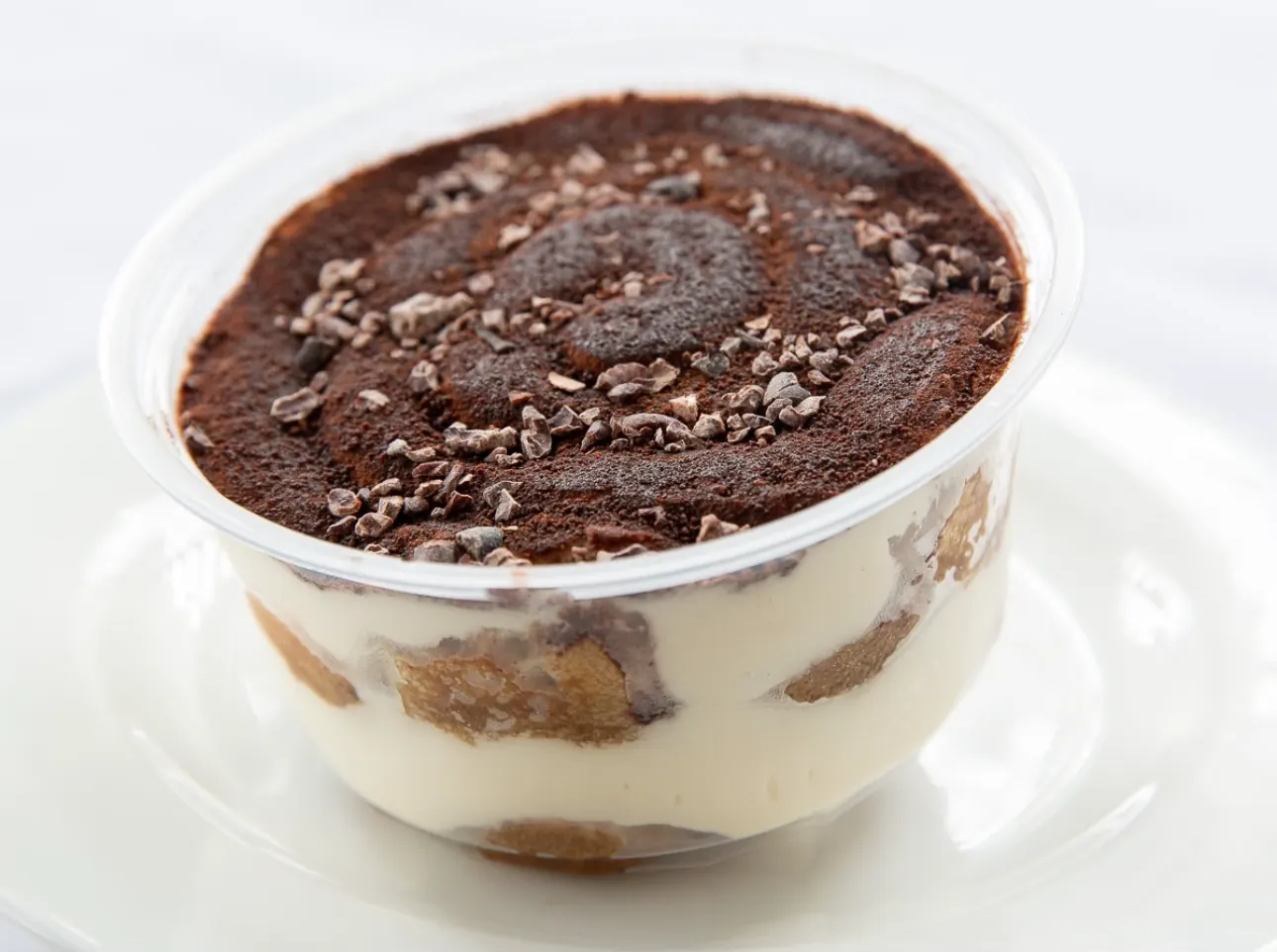 Ali's tiramisu — layers of coffee-soaked biscuit and mascarpone cream in a clear cup, dusted with cocoa and scattered with cacao nibs.