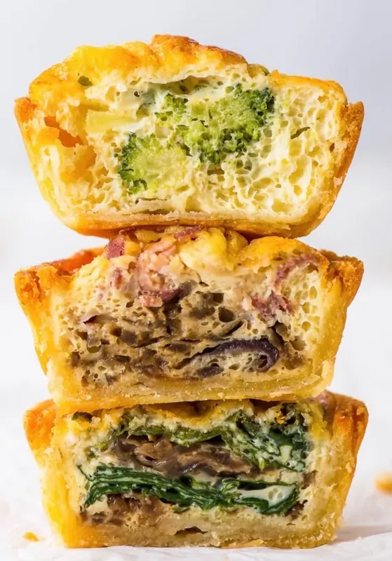 A stack of three mini quiches with golden sablé pastry shells and just-set custard fillings — three rotating savory varieties.