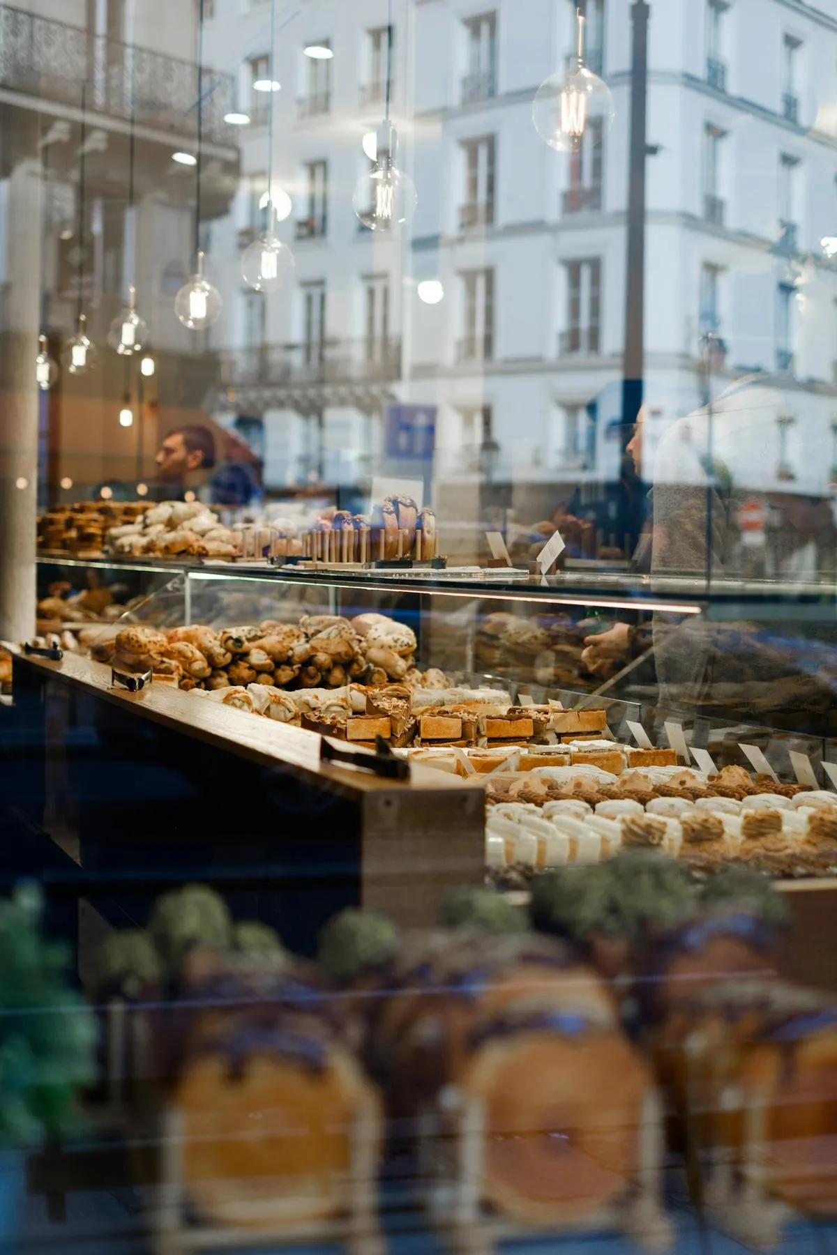 A Parisian patisserie window at golden hour, with reflections of haussmann-era buildings.