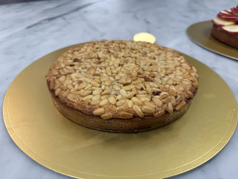 Ali's pine-nut tart — a clean, even layer of toasted pine nuts pressed into a buttery sablé shell on a gold board.