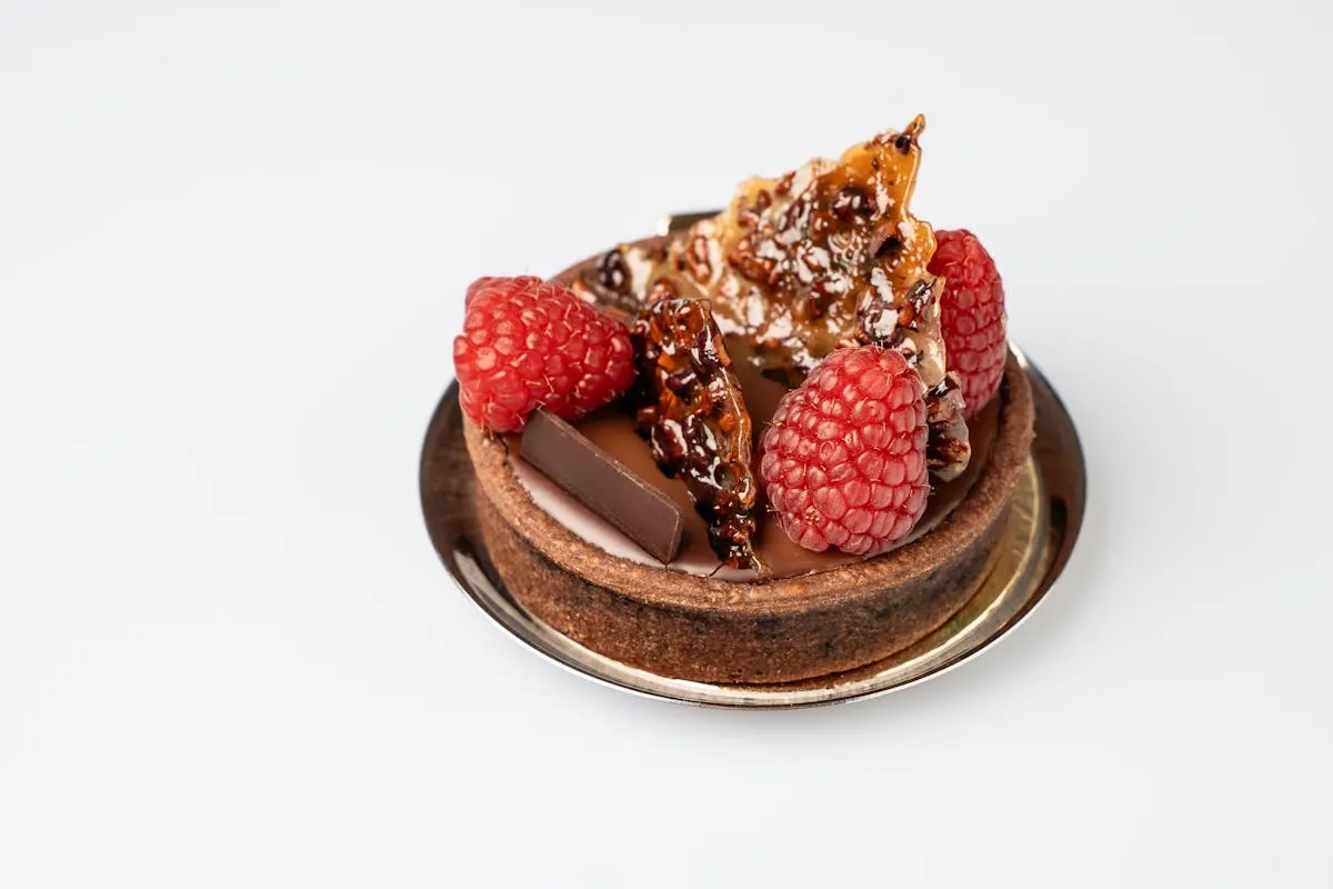 An individual French raspberry-chocolate tartlet with fresh raspberries and a single piece of chocolate — the kind of plated dessert that survives a 300-guest service.